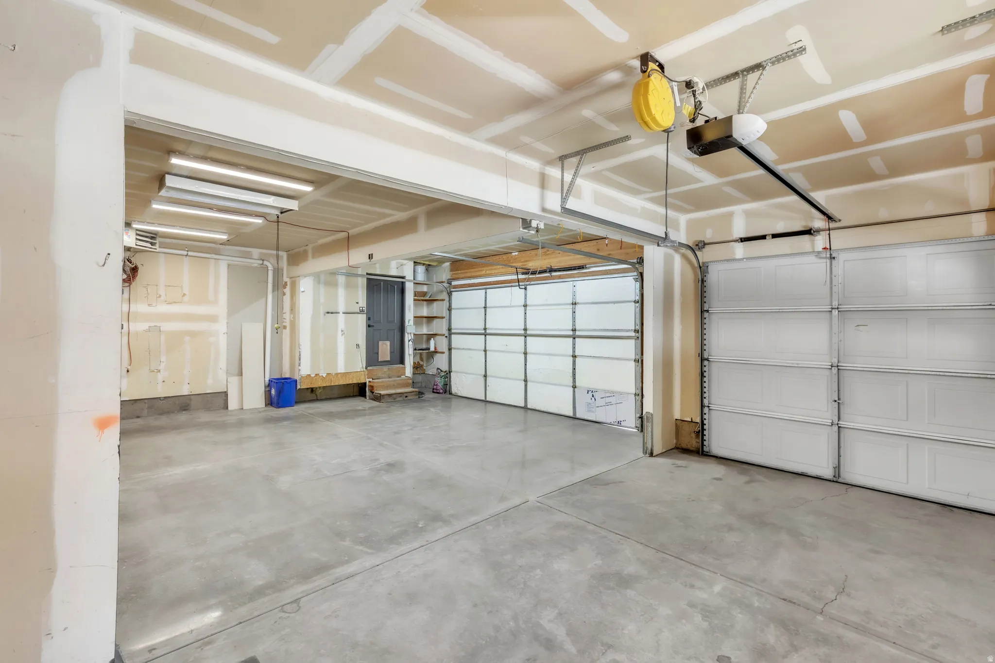 Spacious two-car garage with concrete flooring, fluorescent overhead lighting, and two individual overhead garage doors