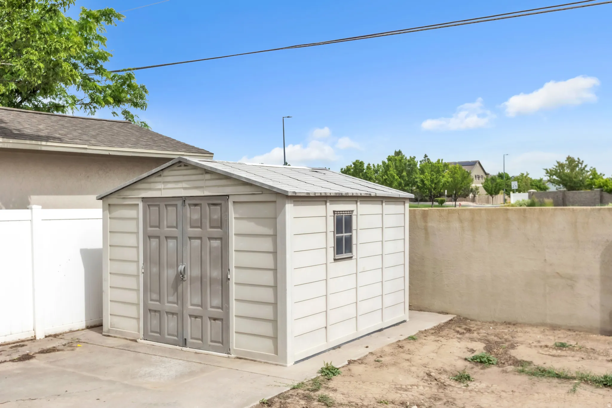 Outdoor storage shed with double doors and a window, situated on a concrete pad