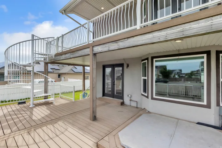 Spacious outdoor deck featuring a spiral staircase, a covered patio area, and a double-door entry