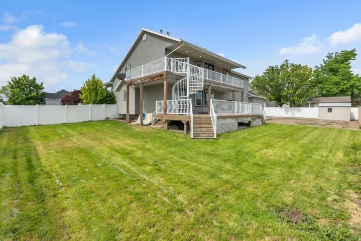 Spacious backyard featuring a two-story stucco exterior, upper and lower decks, a spiral staircase, and a white vinyl fence