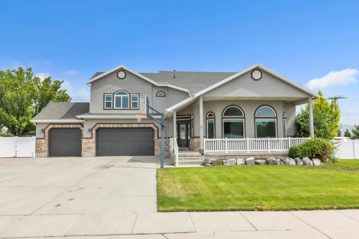 Contemporary residence featuring a two-car garage with stone accents, a covered front porch with white railing, arched windows, and a manicured lawn