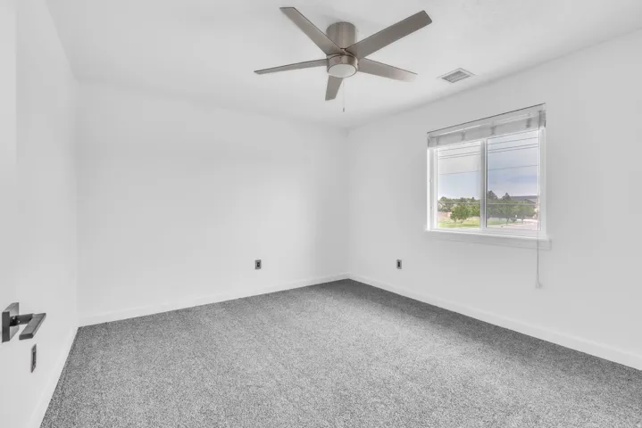 Neutral-toned room featuring a large window with blinds, ceiling fan with brushed nickel accents, and plush grey carpeting