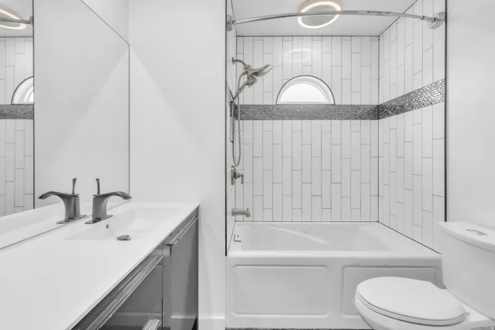 Modern bathroom featuring a full bathtub with subway tile surround, a decorative mosaic tile accent band, and a semi-circular window