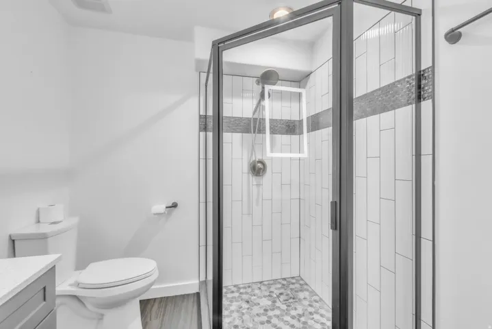 Glass-enclosed shower featuring a black frame, white vertical tile, and a mosaic accent band