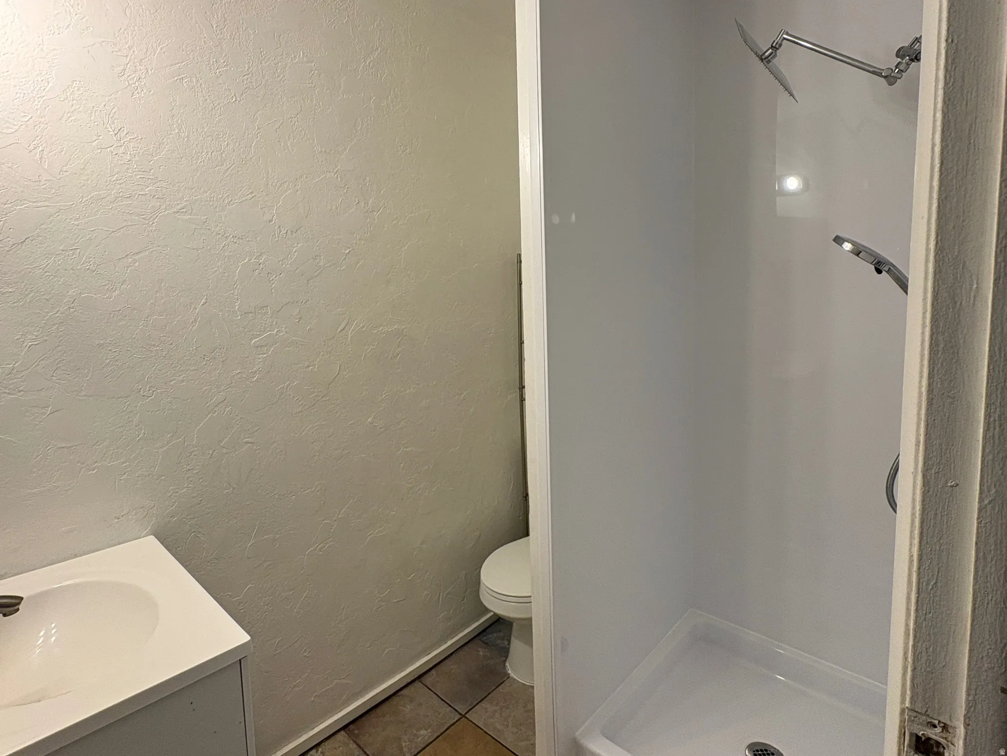 Compact bathroom featuring a white vanity with integrated sink, coordinating toilet, and a stand-up shower with a multi-function showerhead