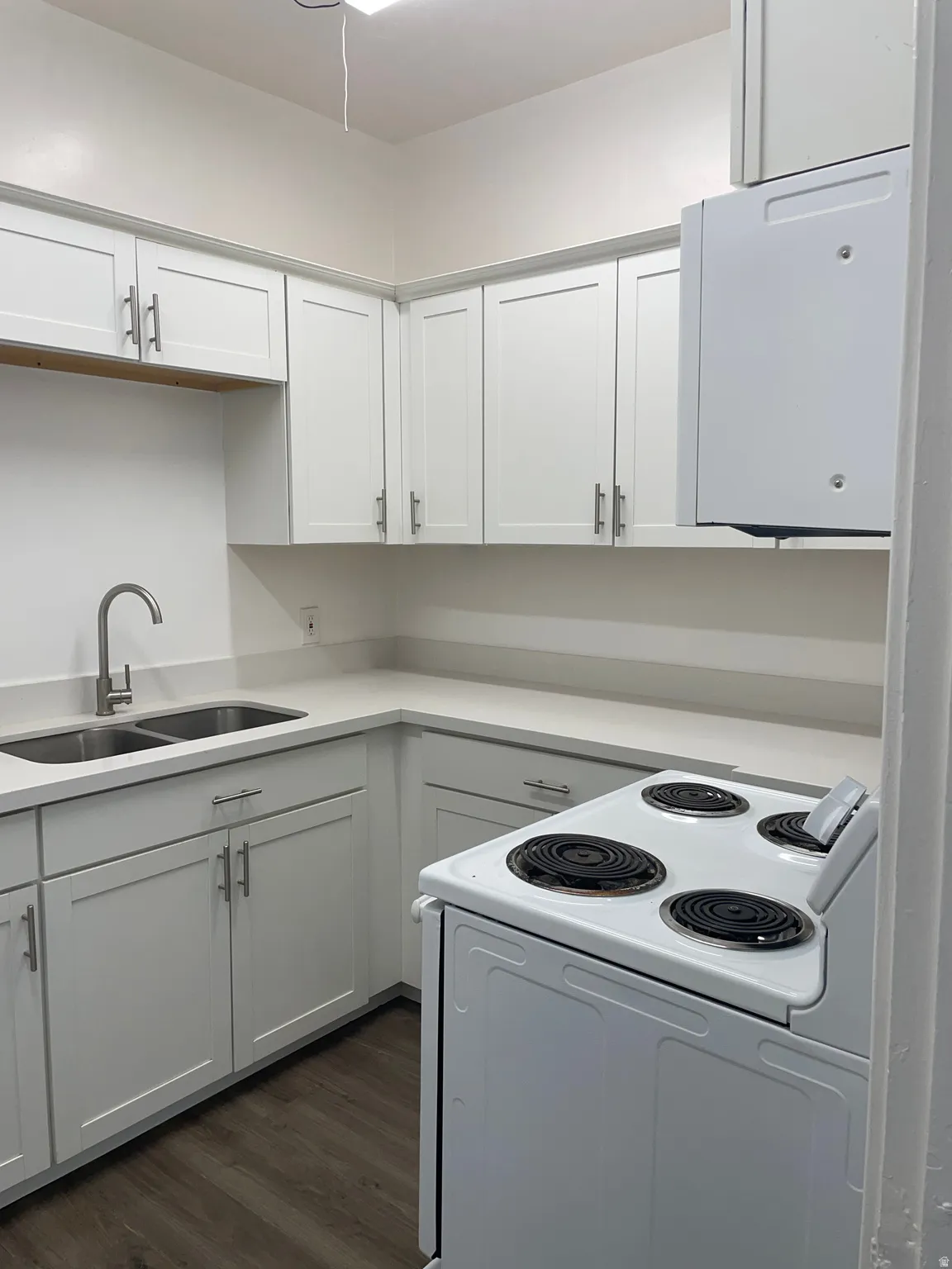 Modern kitchen featuring white shaker cabinetry, light-toned countertops, a double basin sink with a gooseneck faucet, a white electric range, and wood-finish flooring