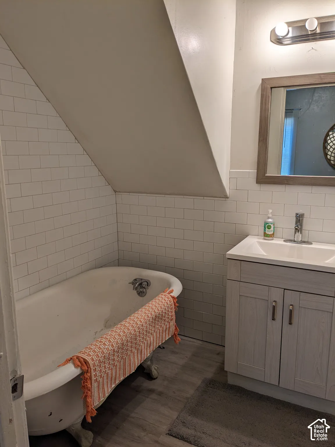 Clawfoot tub with subway tile surround, complementing a vanity with an integrated sink and wood-finish flooring