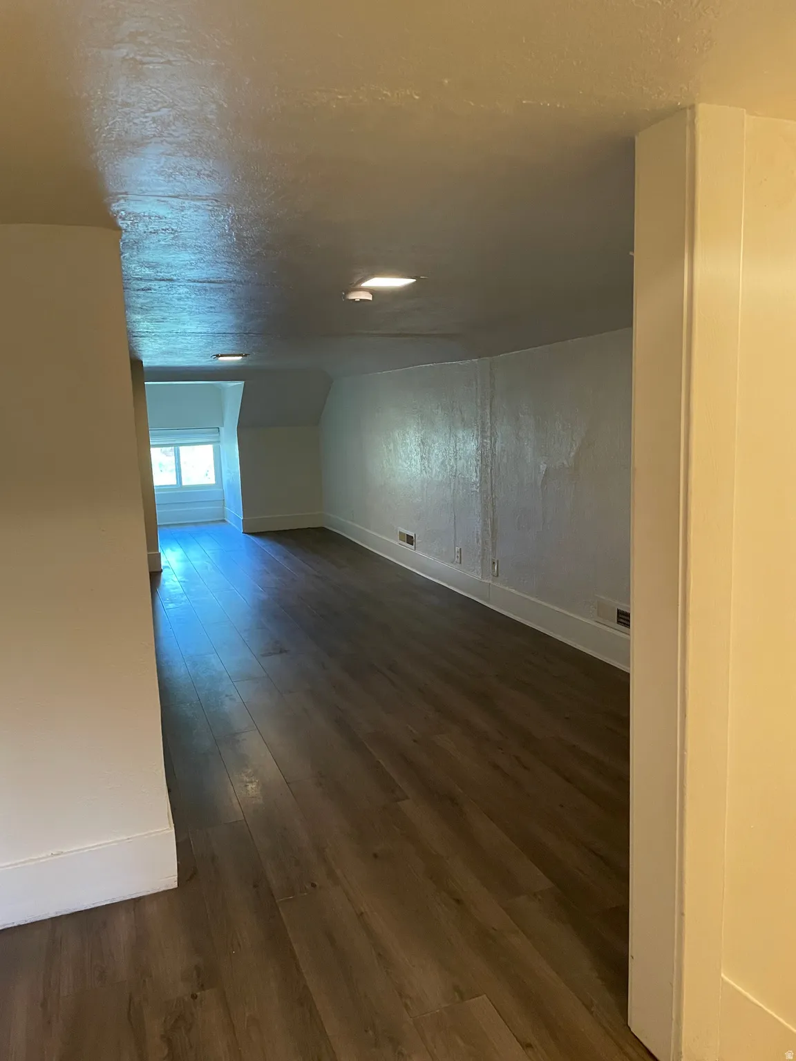 Spacious room featuring wood-finish flooring, white painted walls, recessed lighting, and a large window
