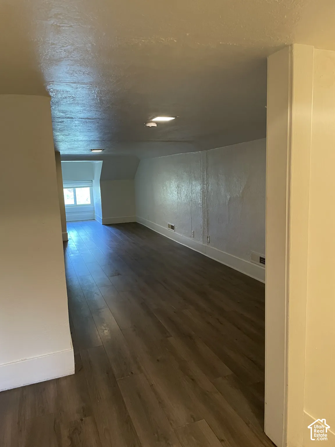 Spacious room featuring wood-finish flooring, white painted walls, recessed lighting, and a large window