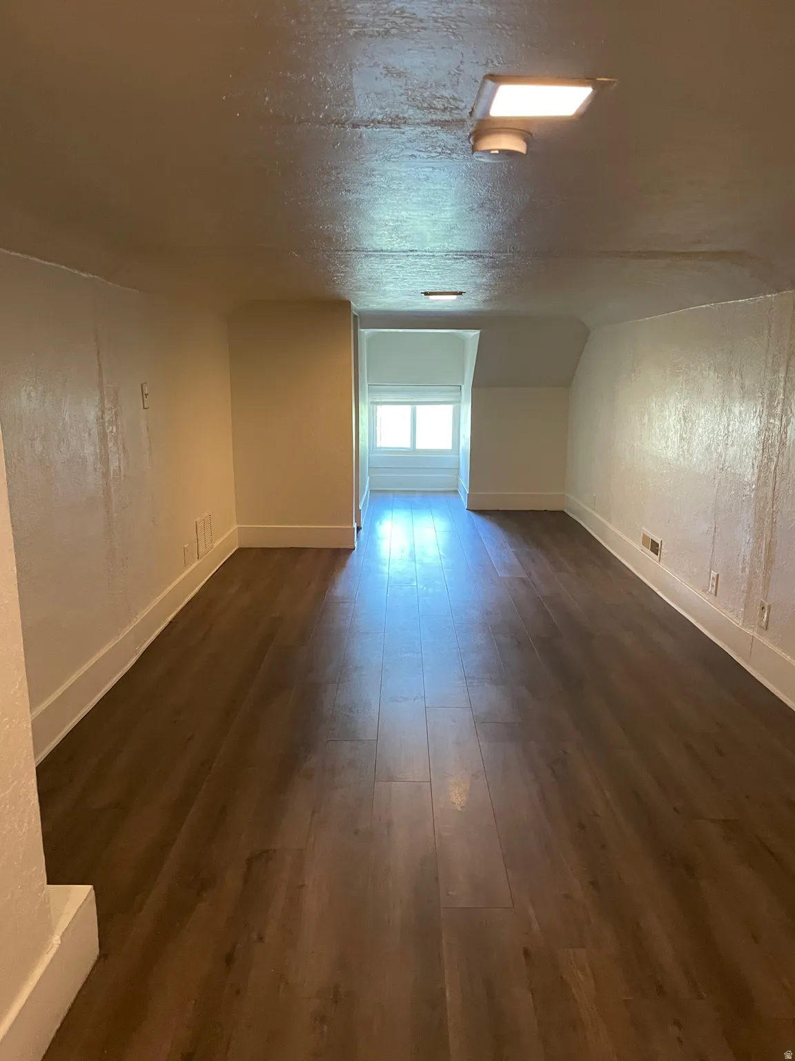 Spacious room featuring wood-finish flooring, white baseboards, and a window providing natural illumination