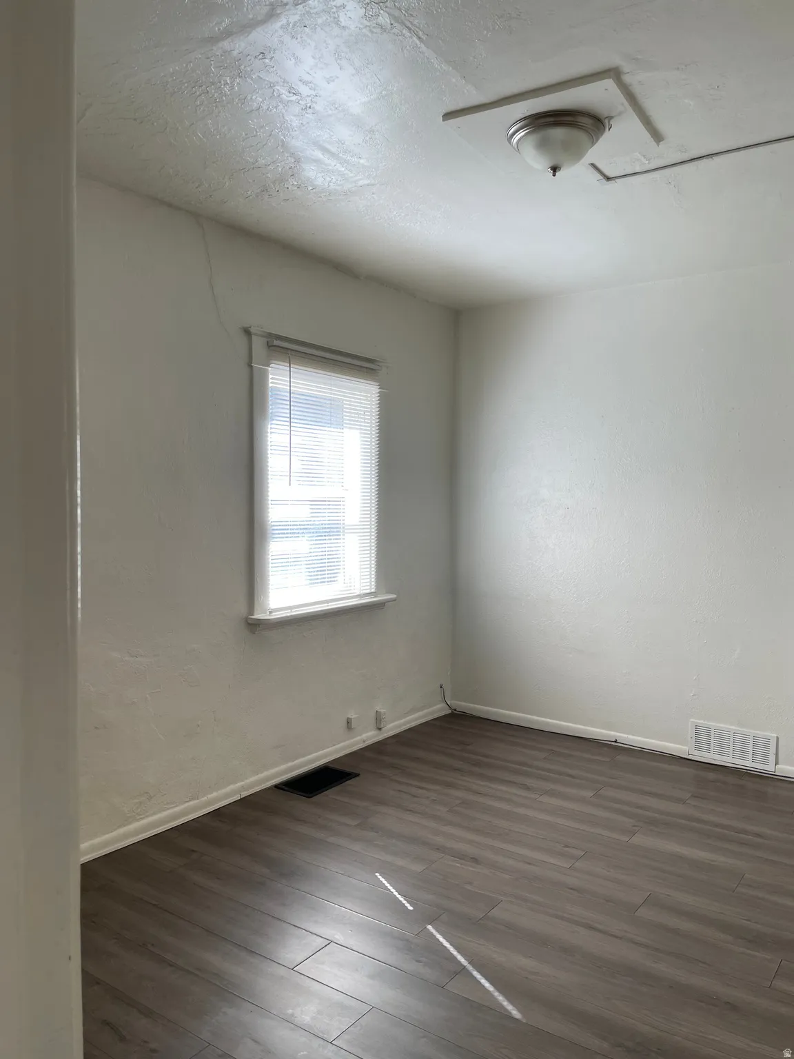 Room featuring wood-finish flooring, white walls, and a single window with blinds