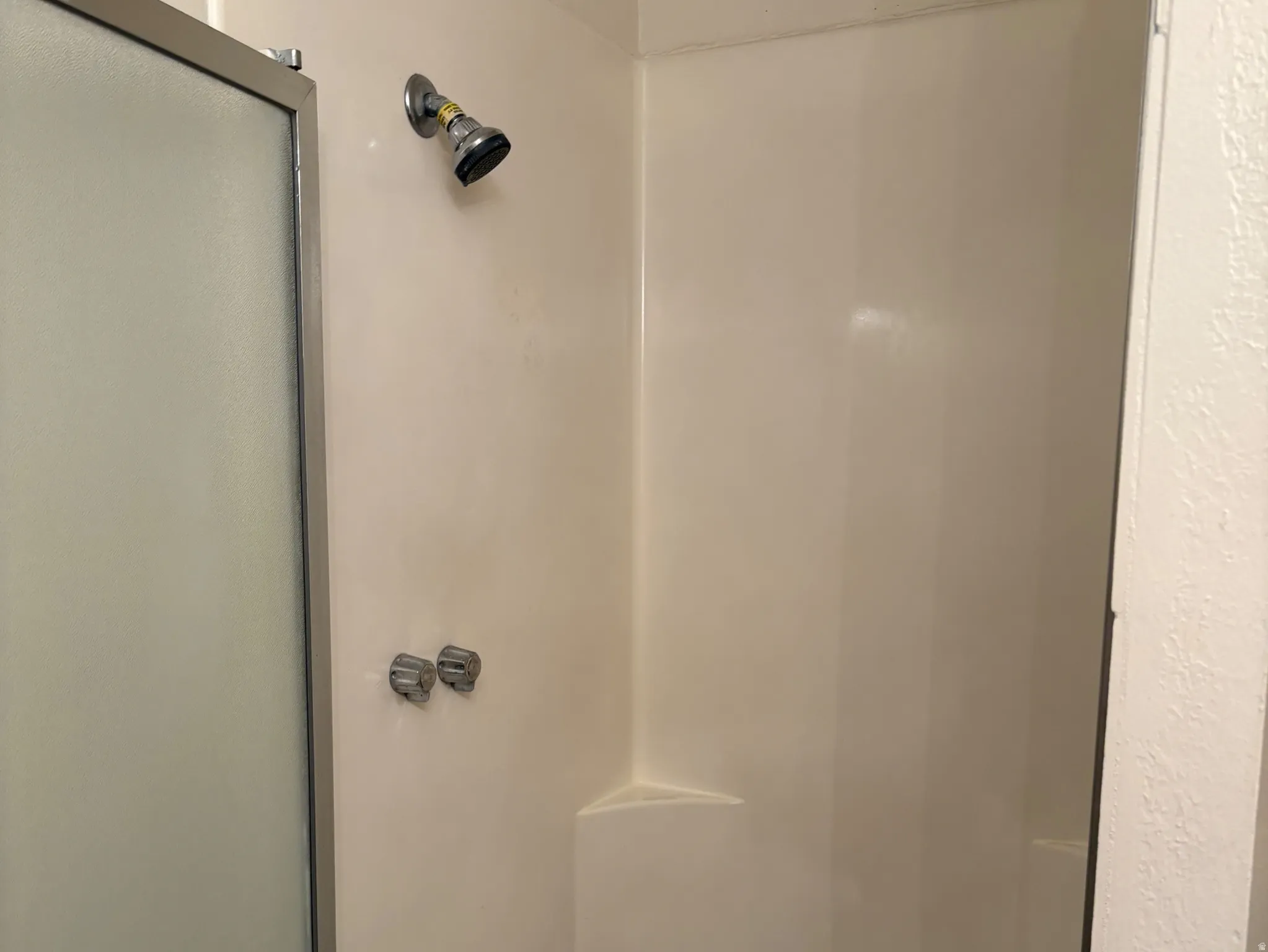 Enclosed shower with a chrome showerhead and control handles, featuring an integrated corner shelf and a sliding frosted glass door