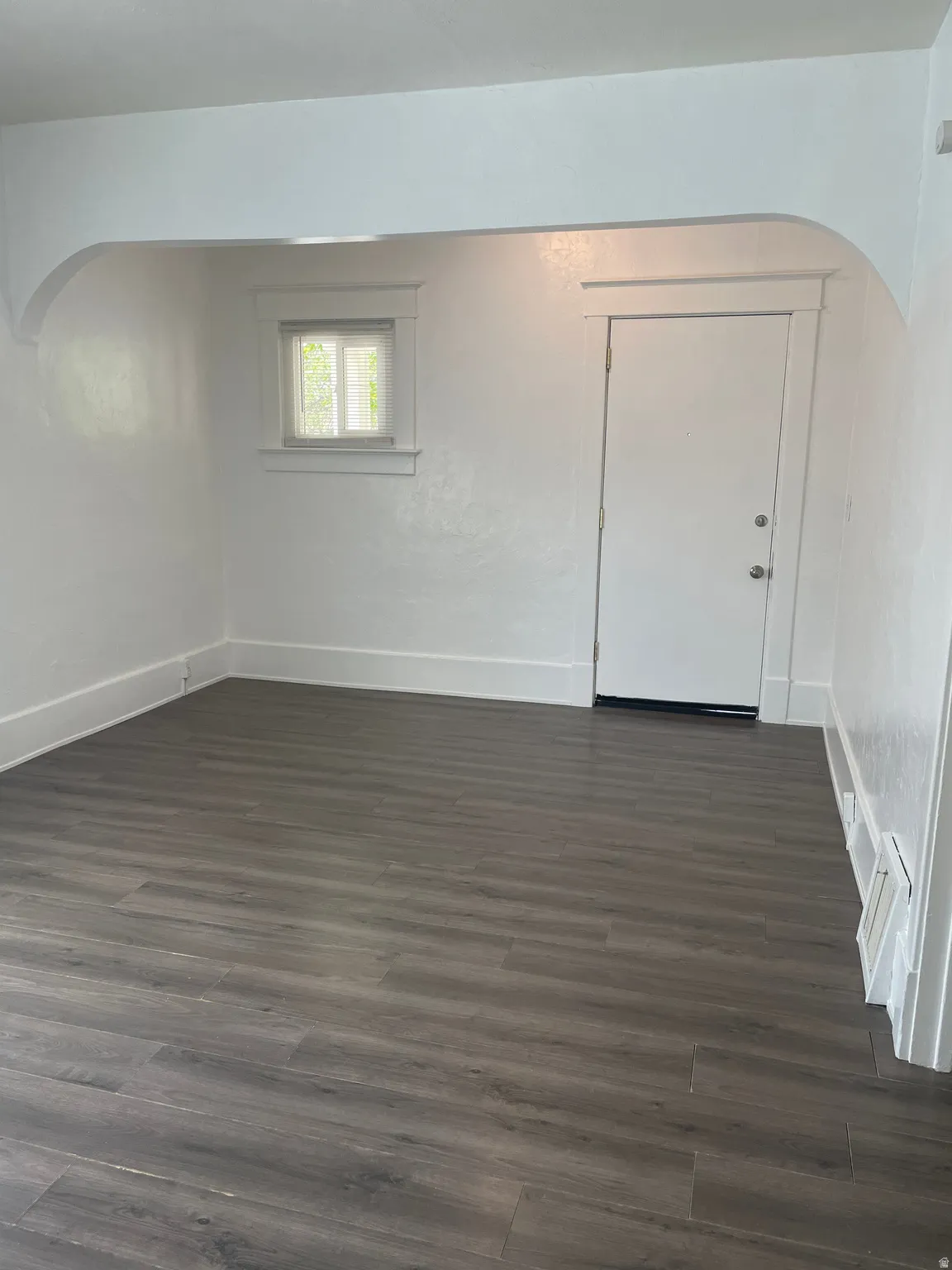 Open room featuring wood-finish flooring, white walls, and an arched entryway