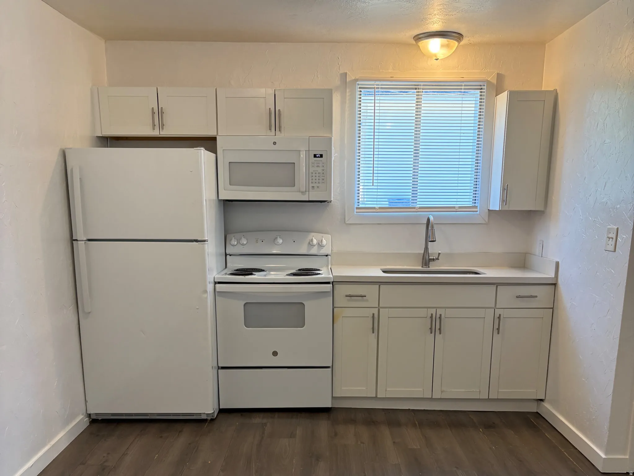 Kitchen featuring wood-finish flooring, white cabinetry, integrated white appliances, and a stainless steel sink with a modern faucet
