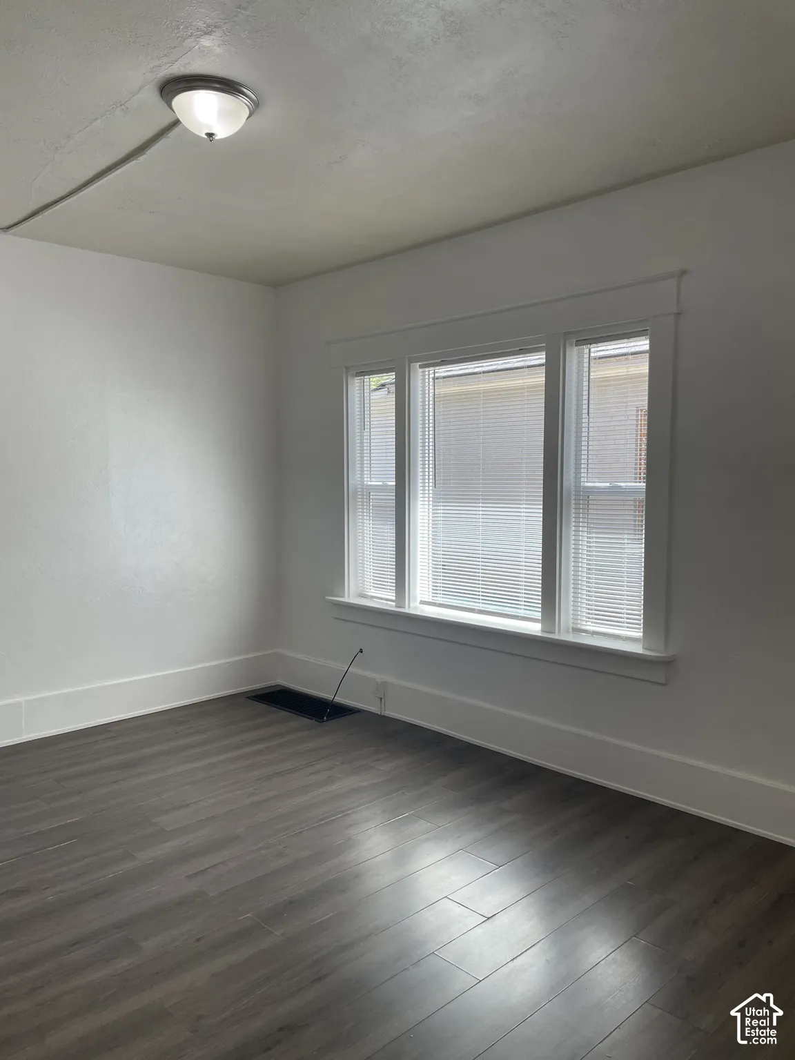 Room featuring large triple window with blinds, wood-finish flooring, white walls, and white trim