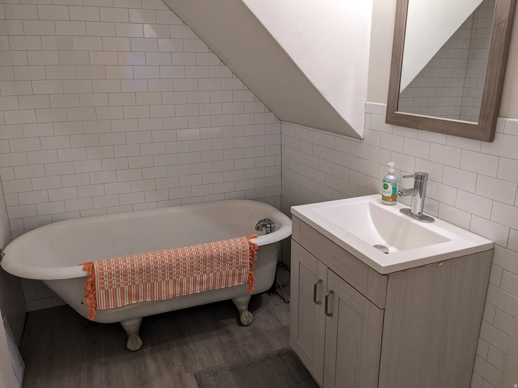Bathroom featuring a clawfoot tub, white subway tile surround, wood-finish flooring, and a vanity with an integrated sink and chrome faucet