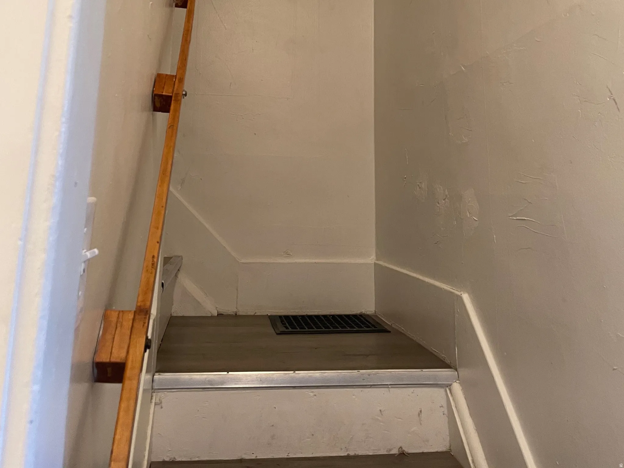 Stairwell featuring a wood handrail, painted walls, white trim, and a floor vent