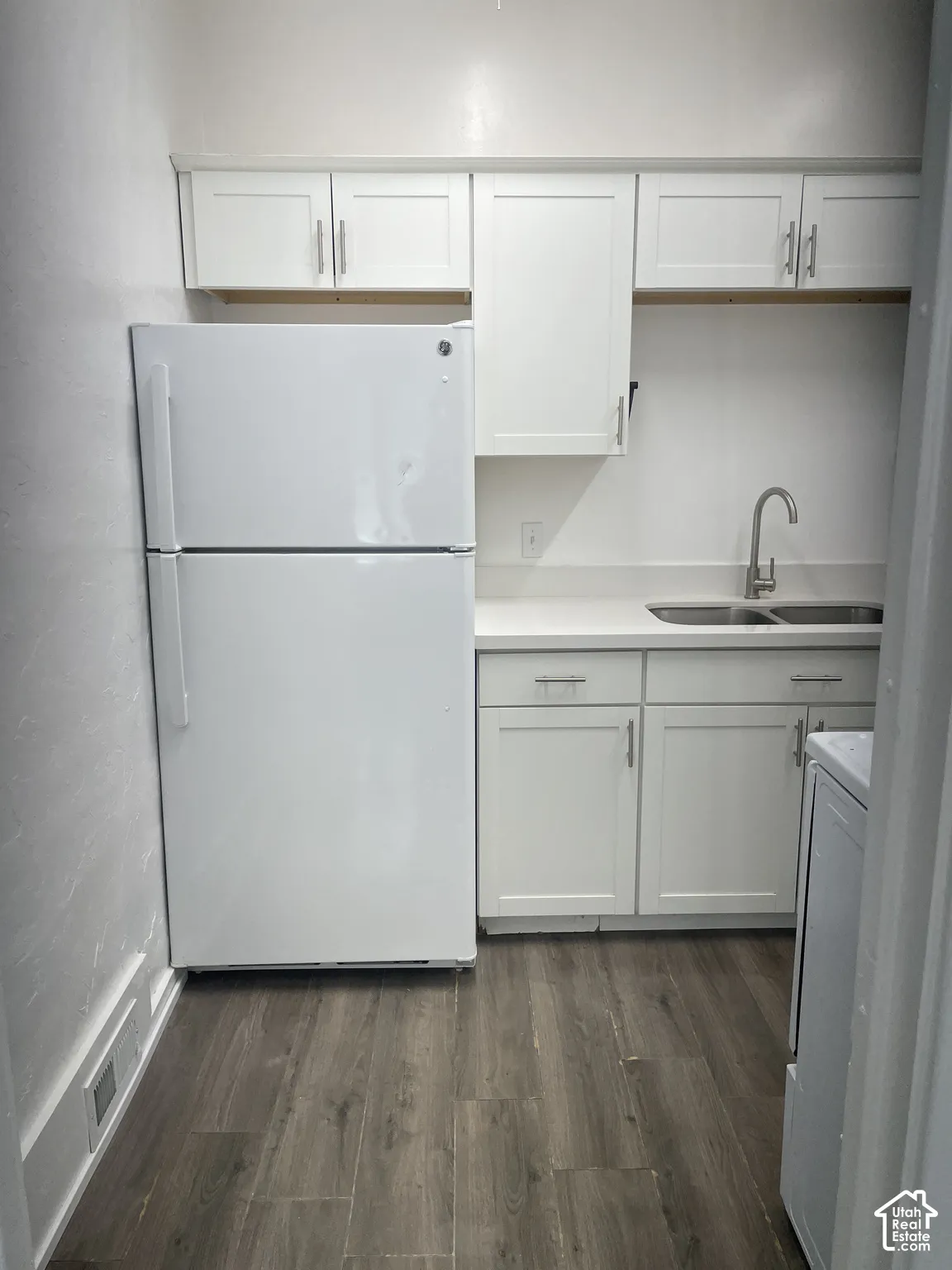 Compact kitchen area featuring white cabinetry, a stainless steel sink with a single-handle faucet, a white refrigerator, and wood-finish flooring