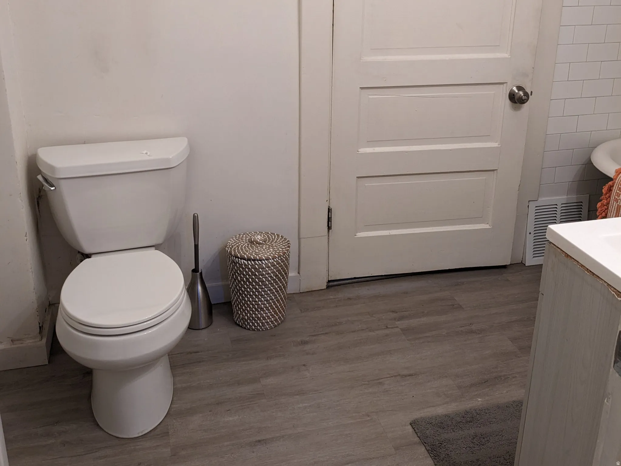 Bathroom with wood-finish flooring, a white toilet, and a white paneled door