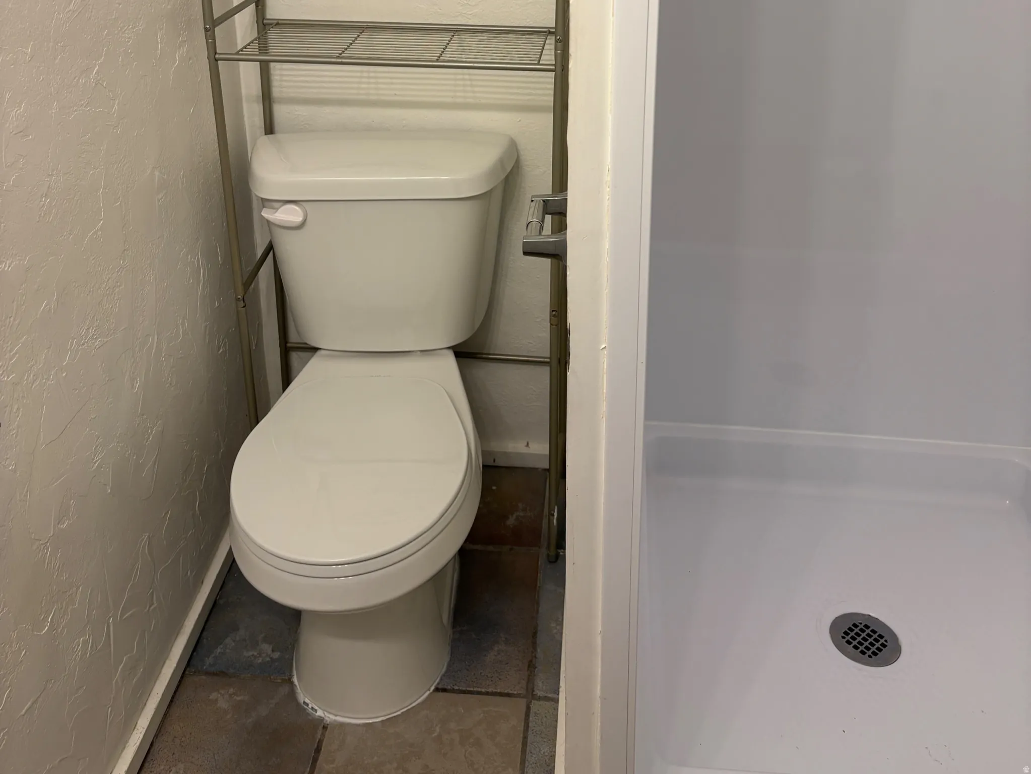 Bathroom featuring a white toilet, tile flooring, and an adjacent shower stall with a white base