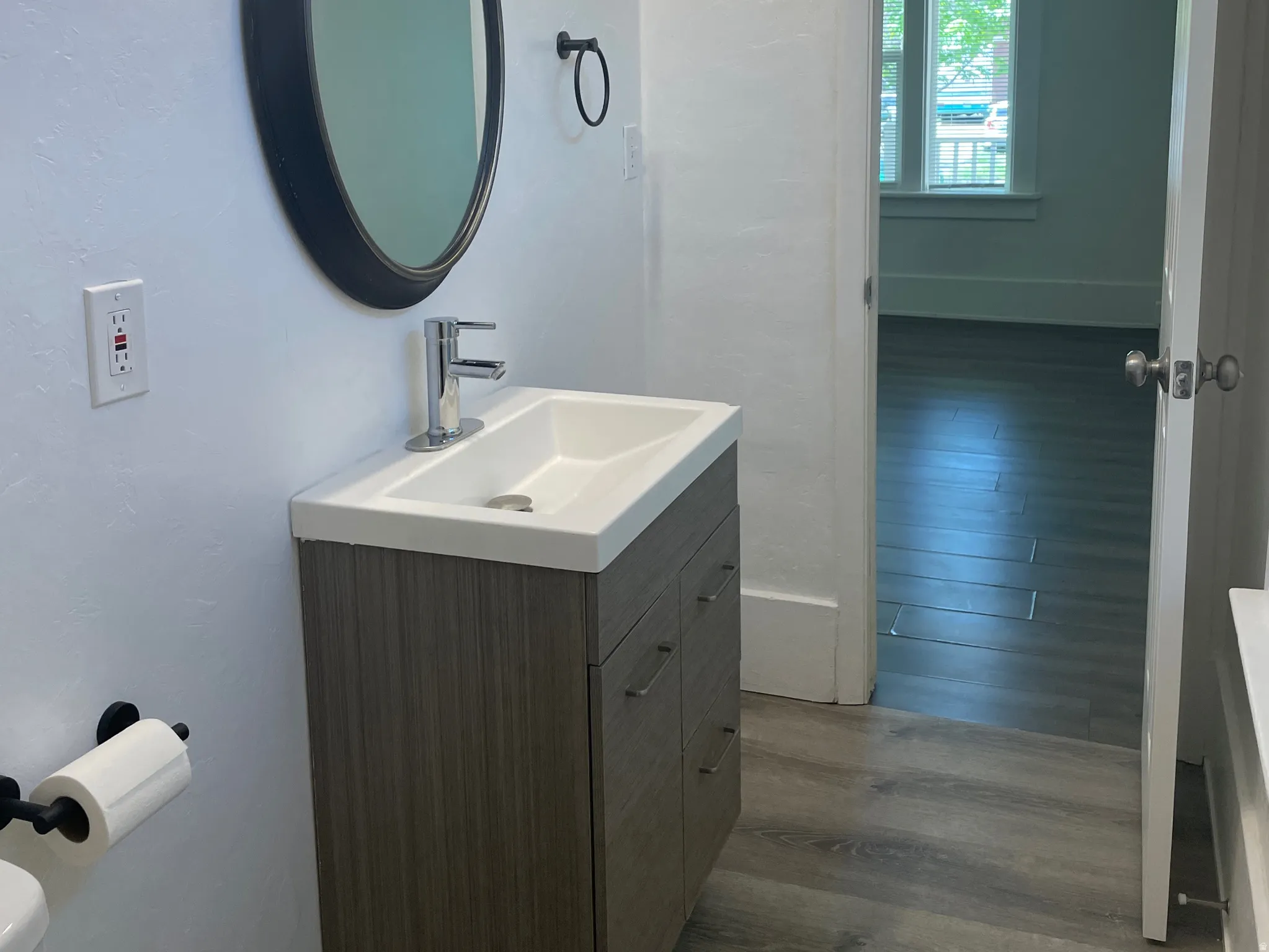 Bathroom featuring a wood-finish vanity with an integrated sink, polished chrome faucet, and a wall-mounted oval mirror