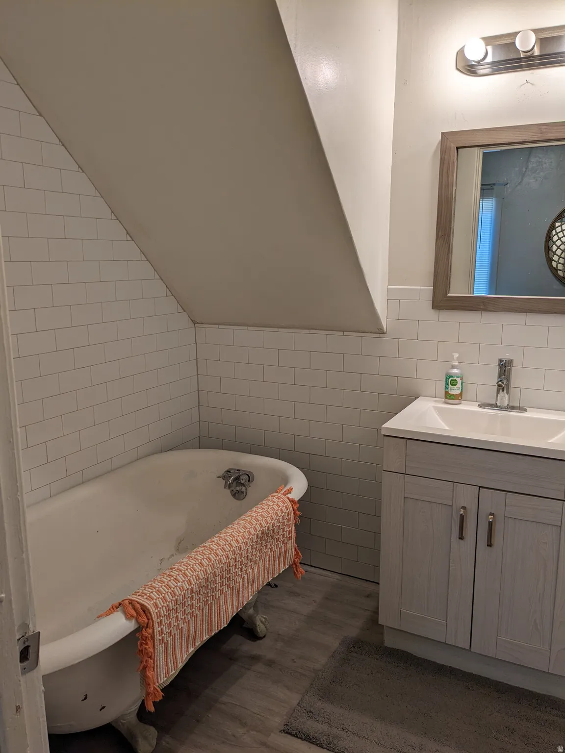 Clawfoot tub with subway tile surround, complementing a vanity with an integrated sink and wood-finish flooring
