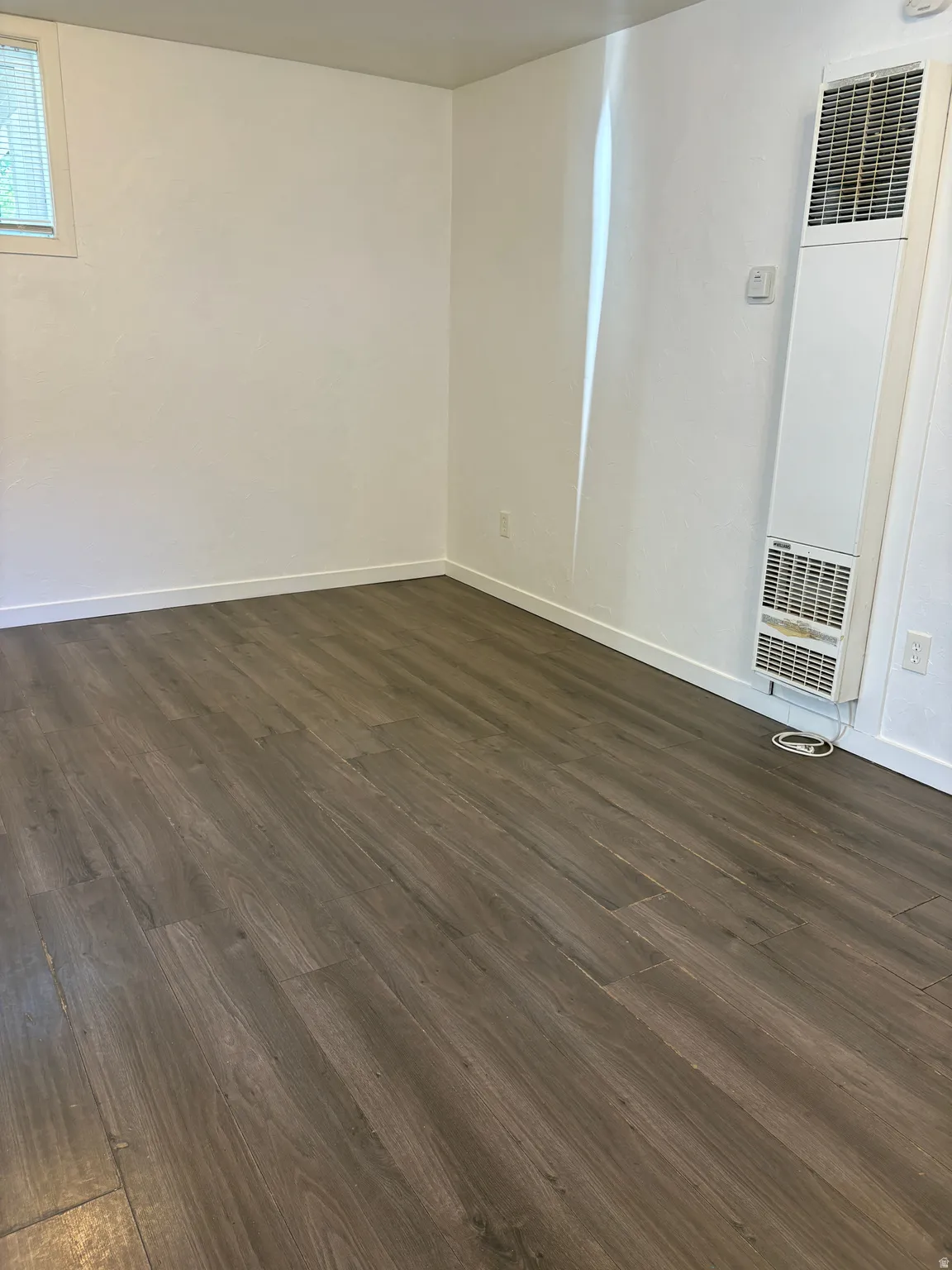 Spacious interior featuring wood-finish flooring, white baseboards, and a window with horizontal blinds