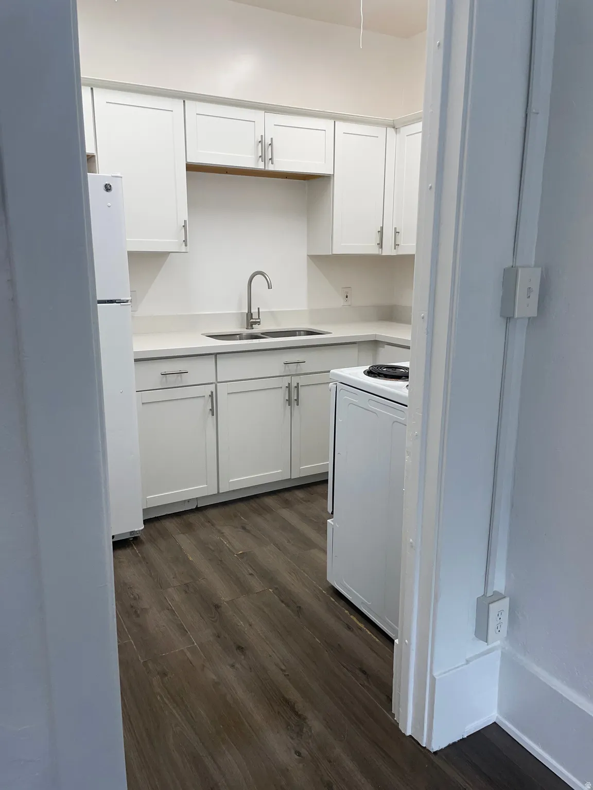 Kitchen featuring white cabinetry, light countertops, a stainless steel sink with a gooseneck faucet, a white refrigerator, and wood-finish flooring