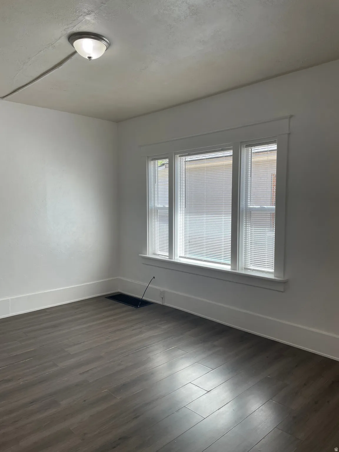 Room featuring large triple window with blinds, wood-finish flooring, white walls, and white trim