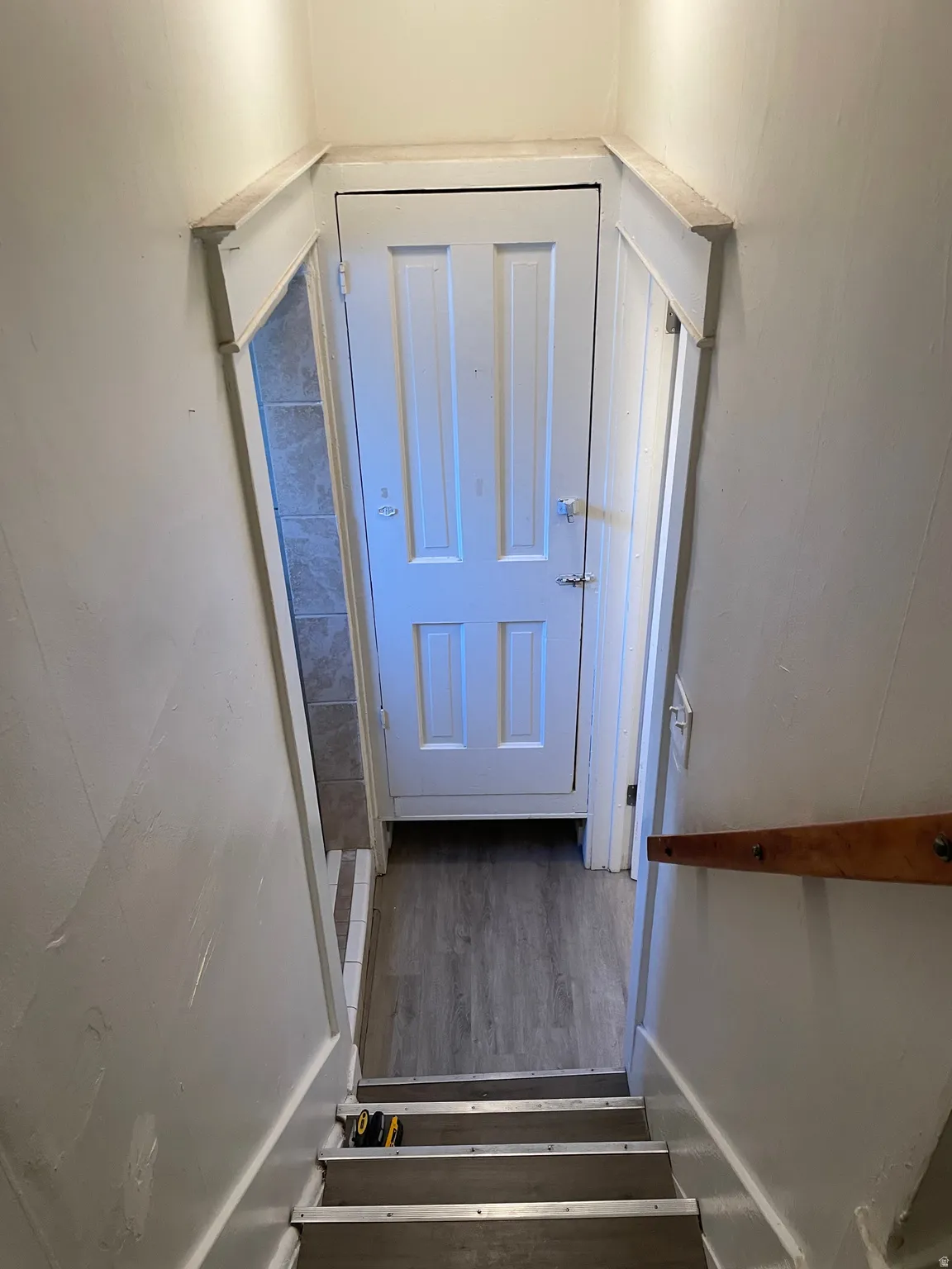 White paneled door with a privacy lock, wood-finish flooring, and light gray wall tiling