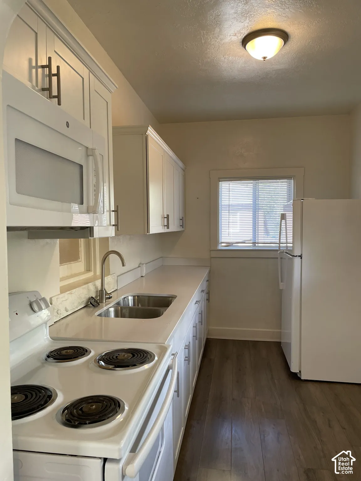 Kitchen featuring white cabinetry with dark hardware, a white oven, a stainless steel double basin sink, and wood-finish flooring