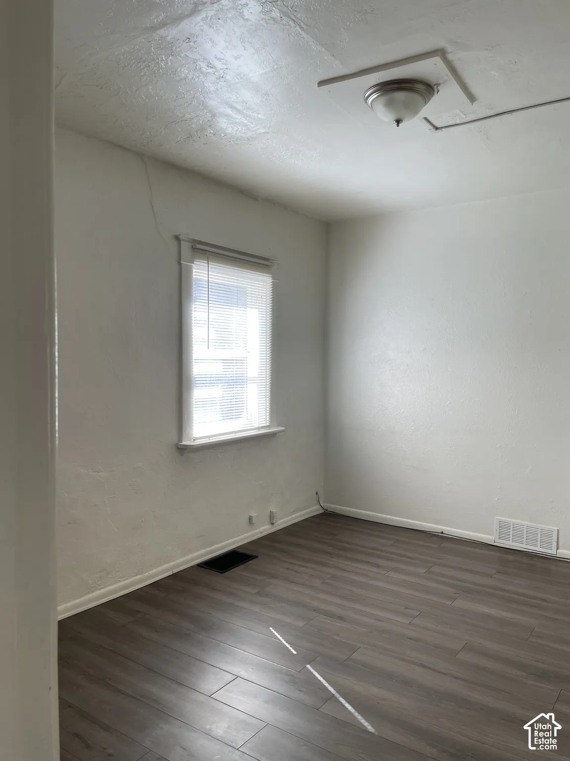 Room featuring wood-finish flooring, white walls, and a single window with blinds