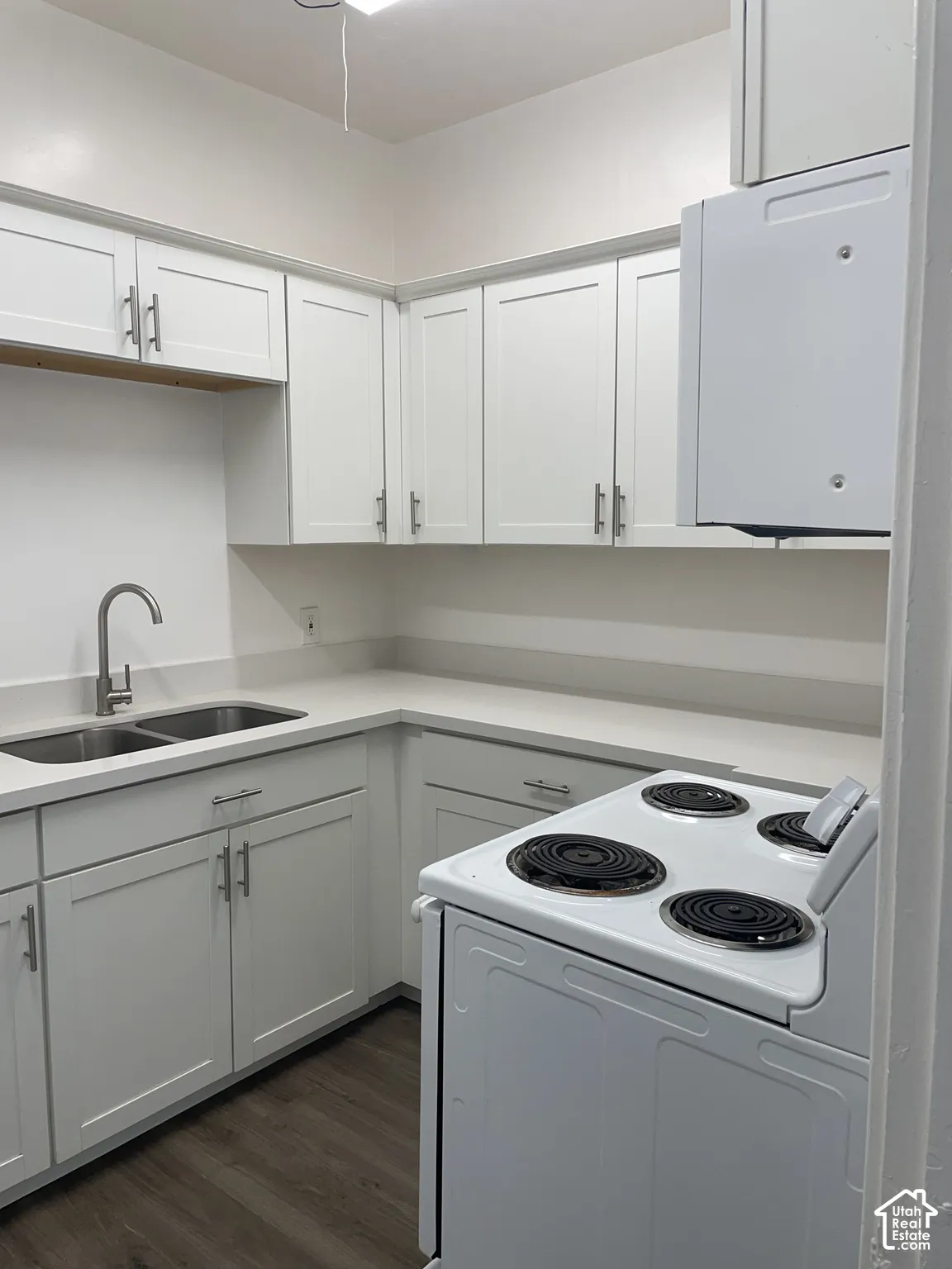 Modern kitchen featuring white shaker cabinetry, light-toned countertops, a double basin sink with a gooseneck faucet, a white electric range, and wood-finish flooring