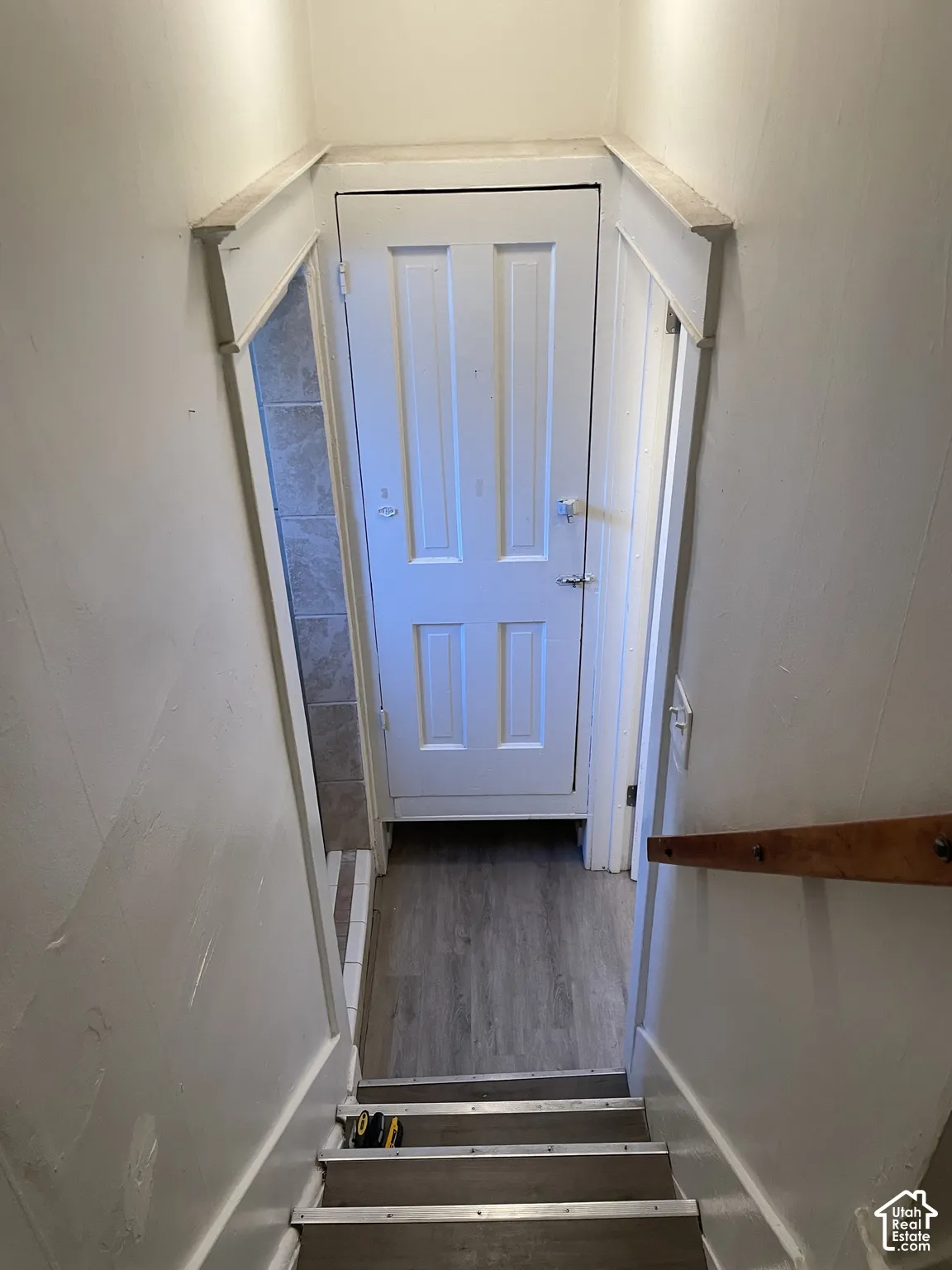 White paneled door with a privacy lock, wood-finish flooring, and light gray wall tiling