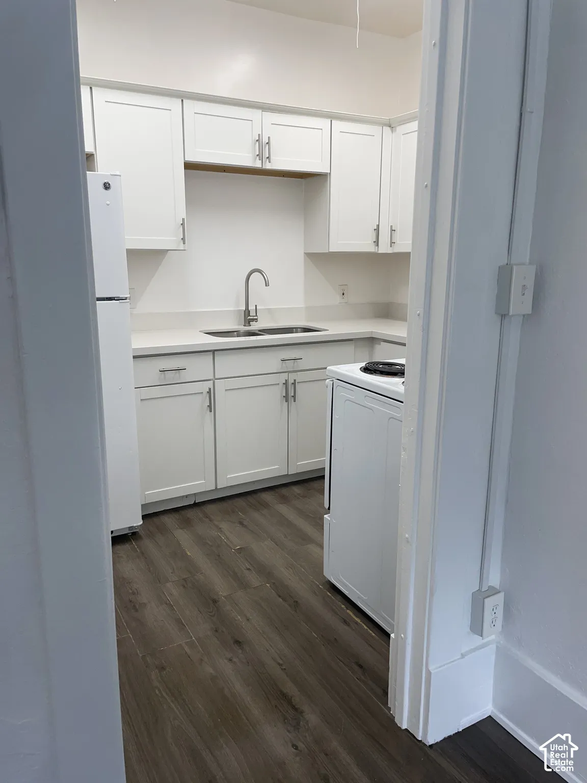 Kitchen featuring white cabinetry, light countertops, a stainless steel sink with a gooseneck faucet, a white refrigerator, and wood-finish flooring