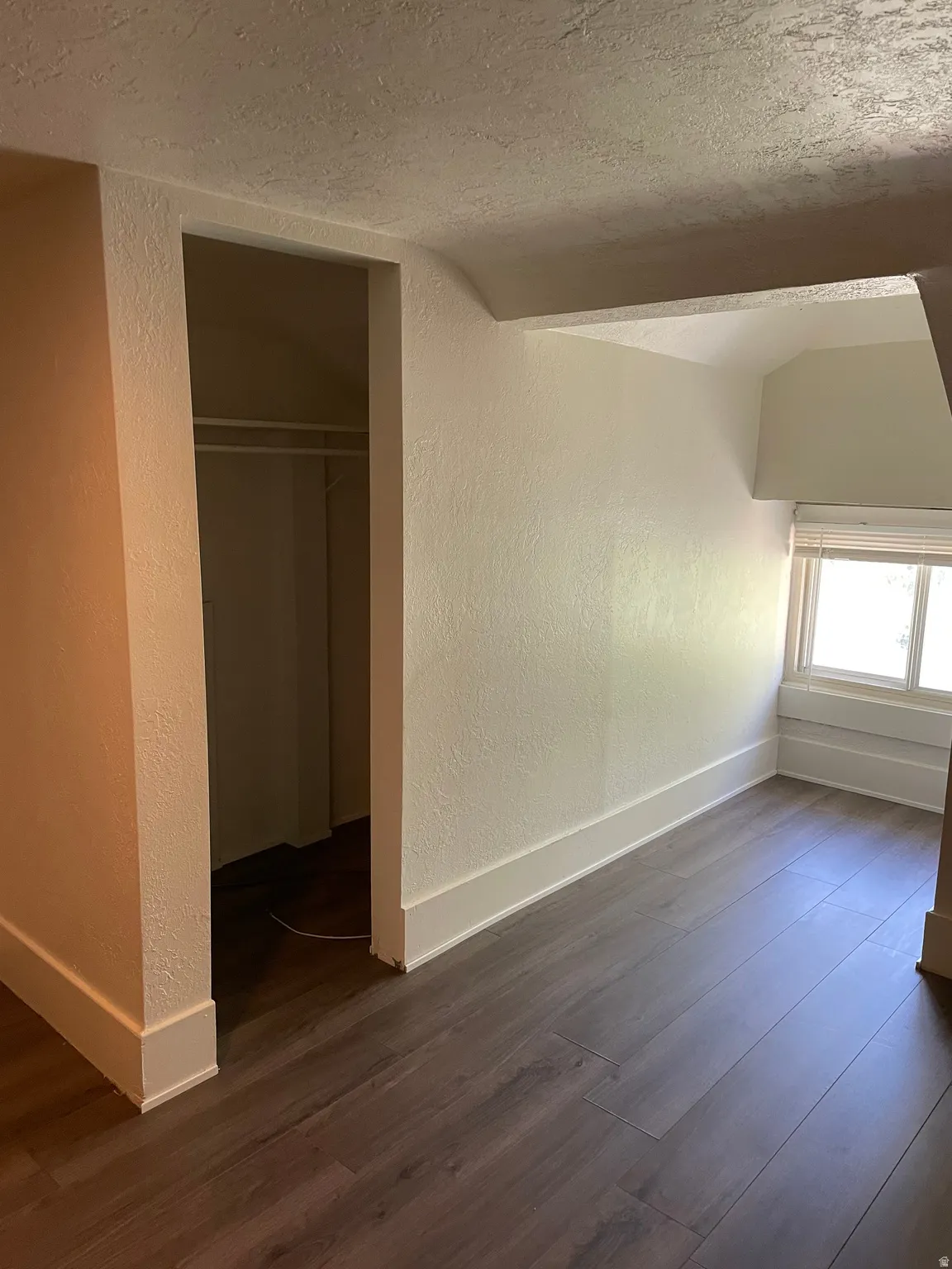 Room featuring wood-finish flooring, white baseboards, light-colored walls, and a window with blinds