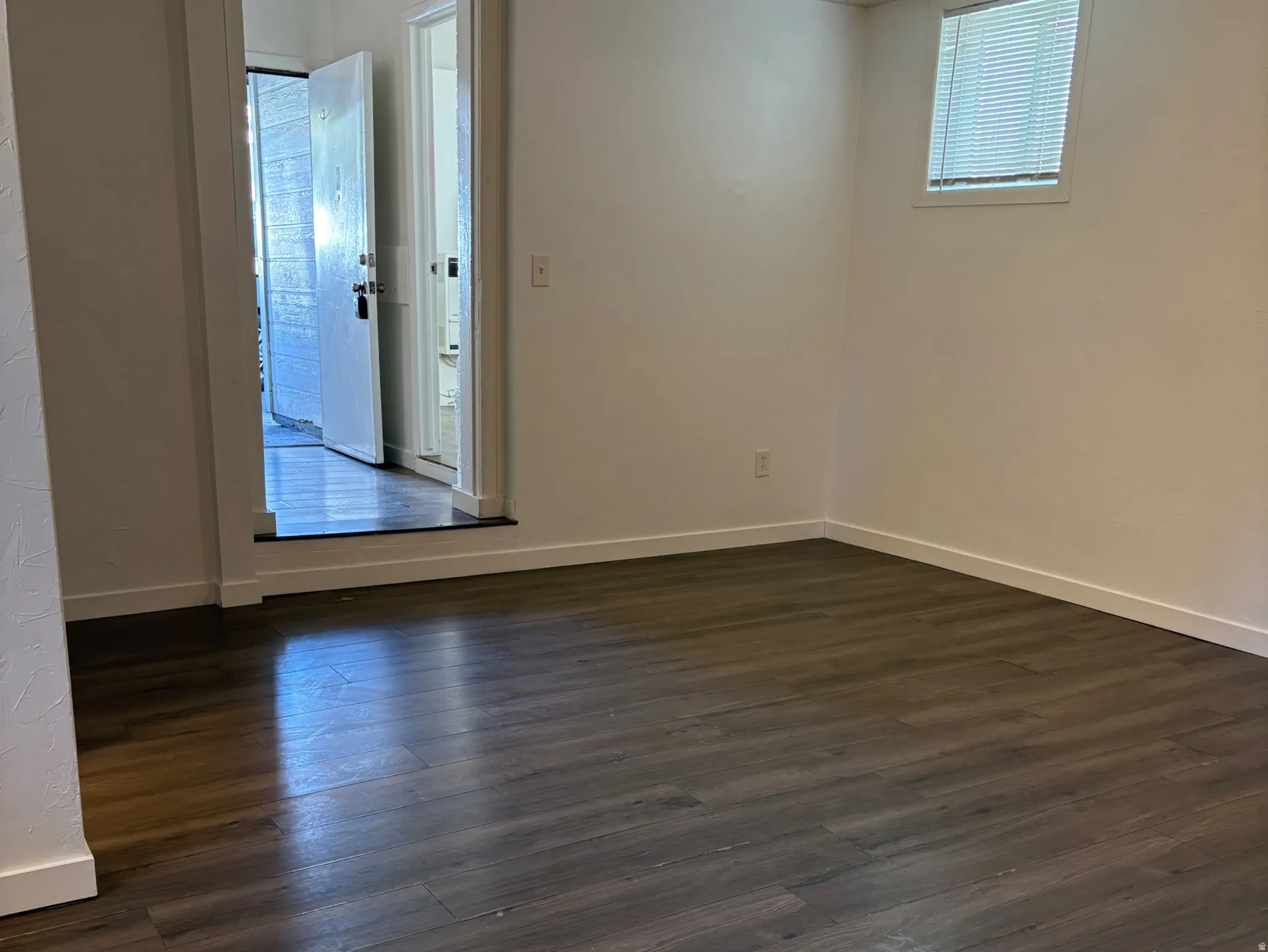 Spacious room featuring dark wood-finish flooring, white baseboards, and freshly painted white walls