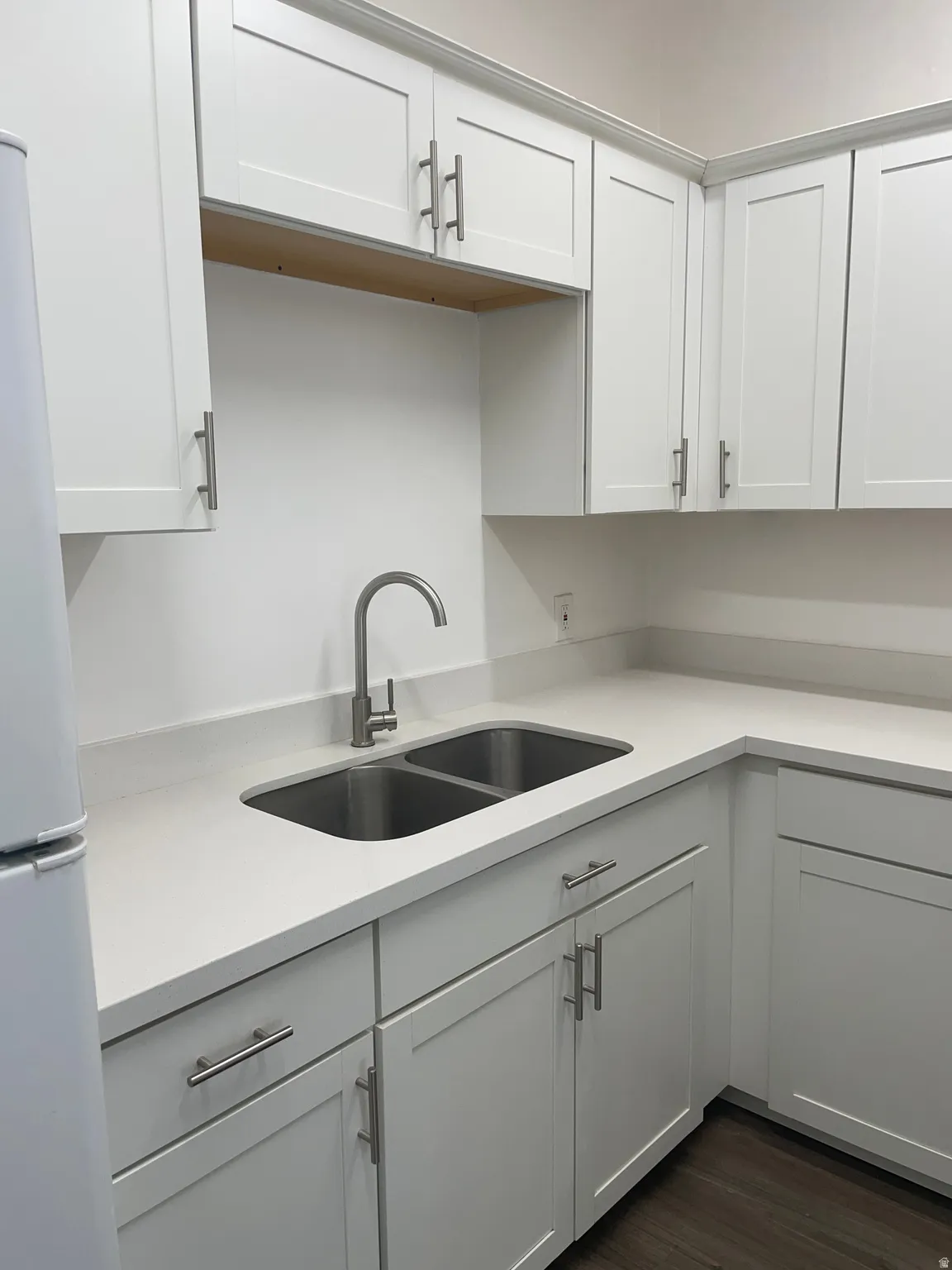 Kitchen featuring white shaker-style cabinetry, light-toned countertops, a stainless steel double-basin sink, and a high-arc faucet