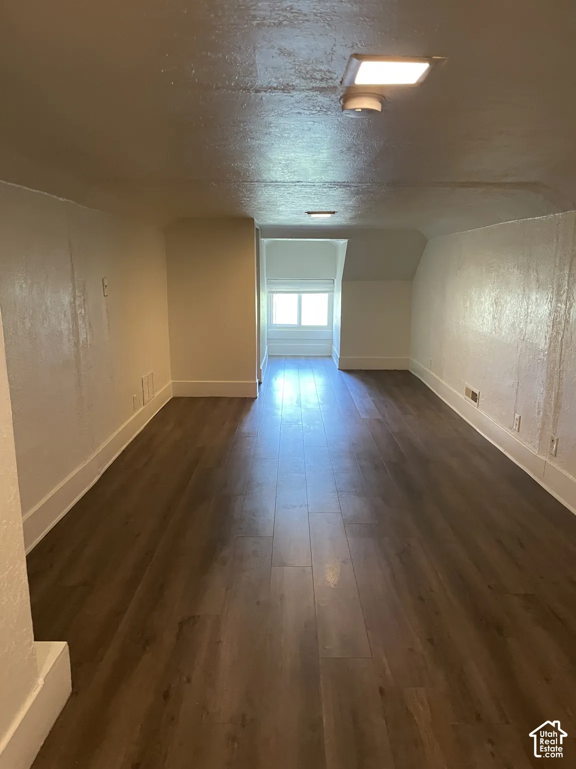 Spacious room featuring wood-finish flooring, white baseboards, and a window providing natural illumination