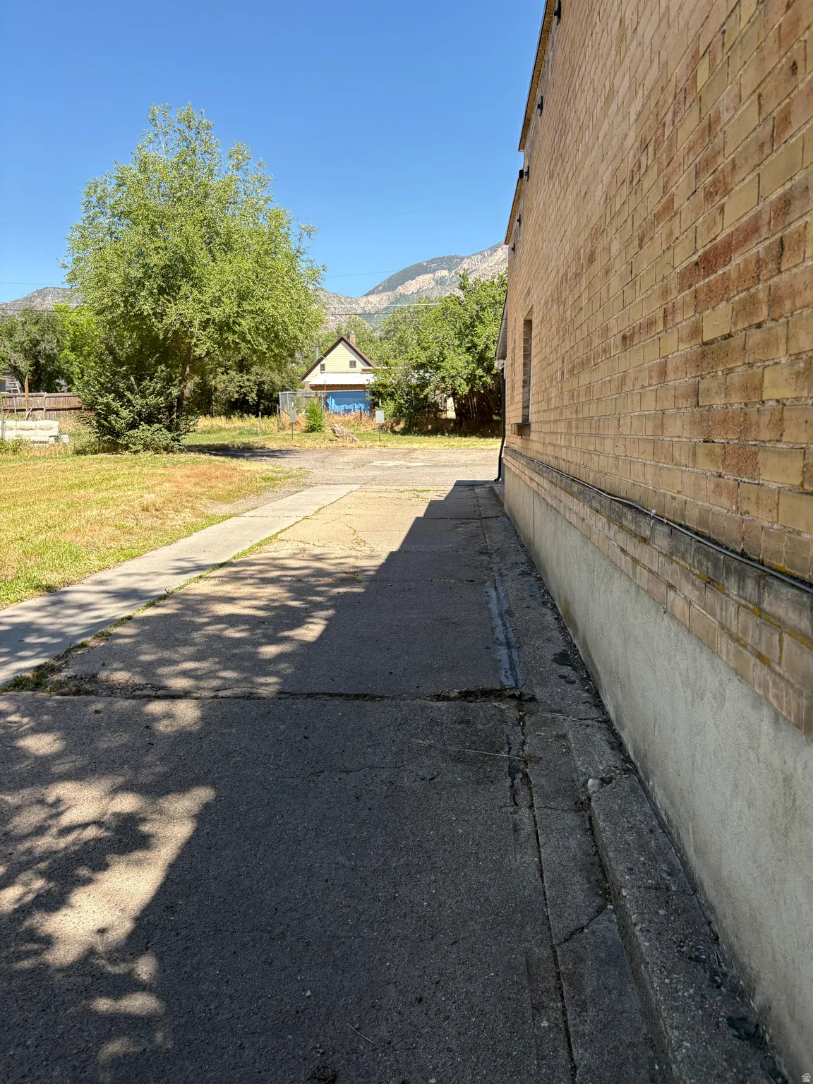 Brick exterior with concrete foundation, featuring a paved pathway and an expansive grassy area