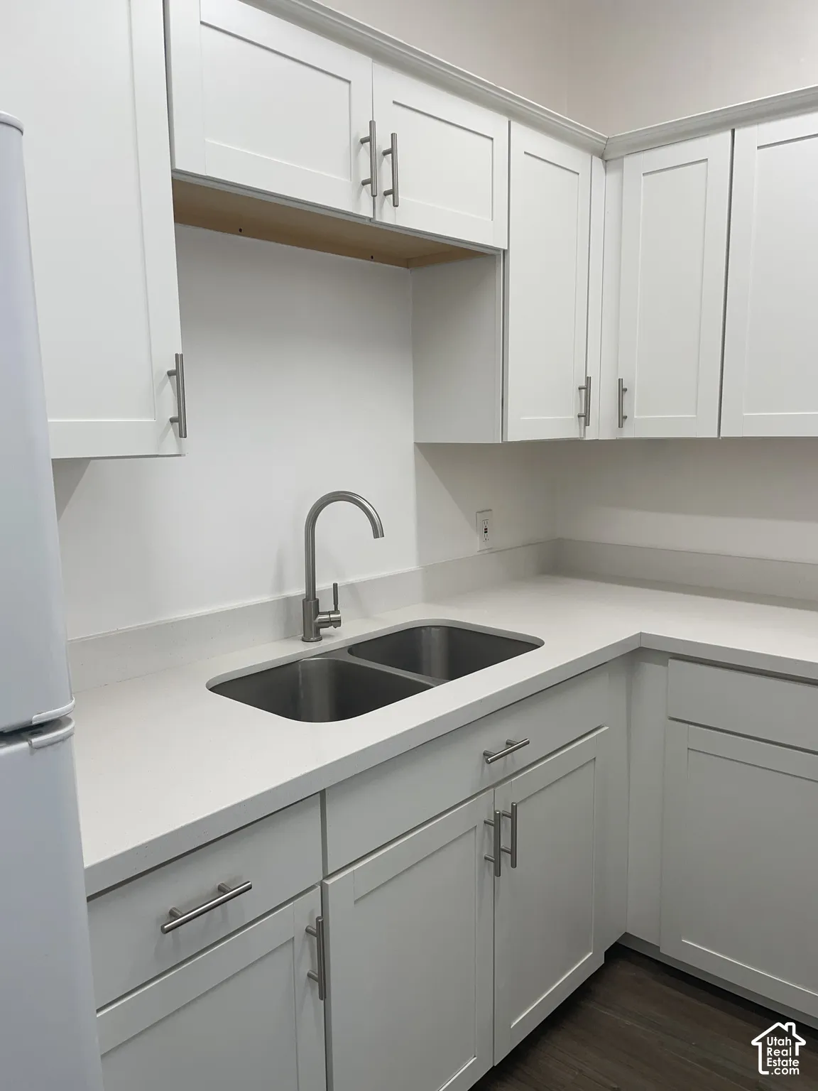 Kitchen featuring white shaker-style cabinetry, light-toned countertops, a stainless steel double-basin sink, and a high-arc faucet