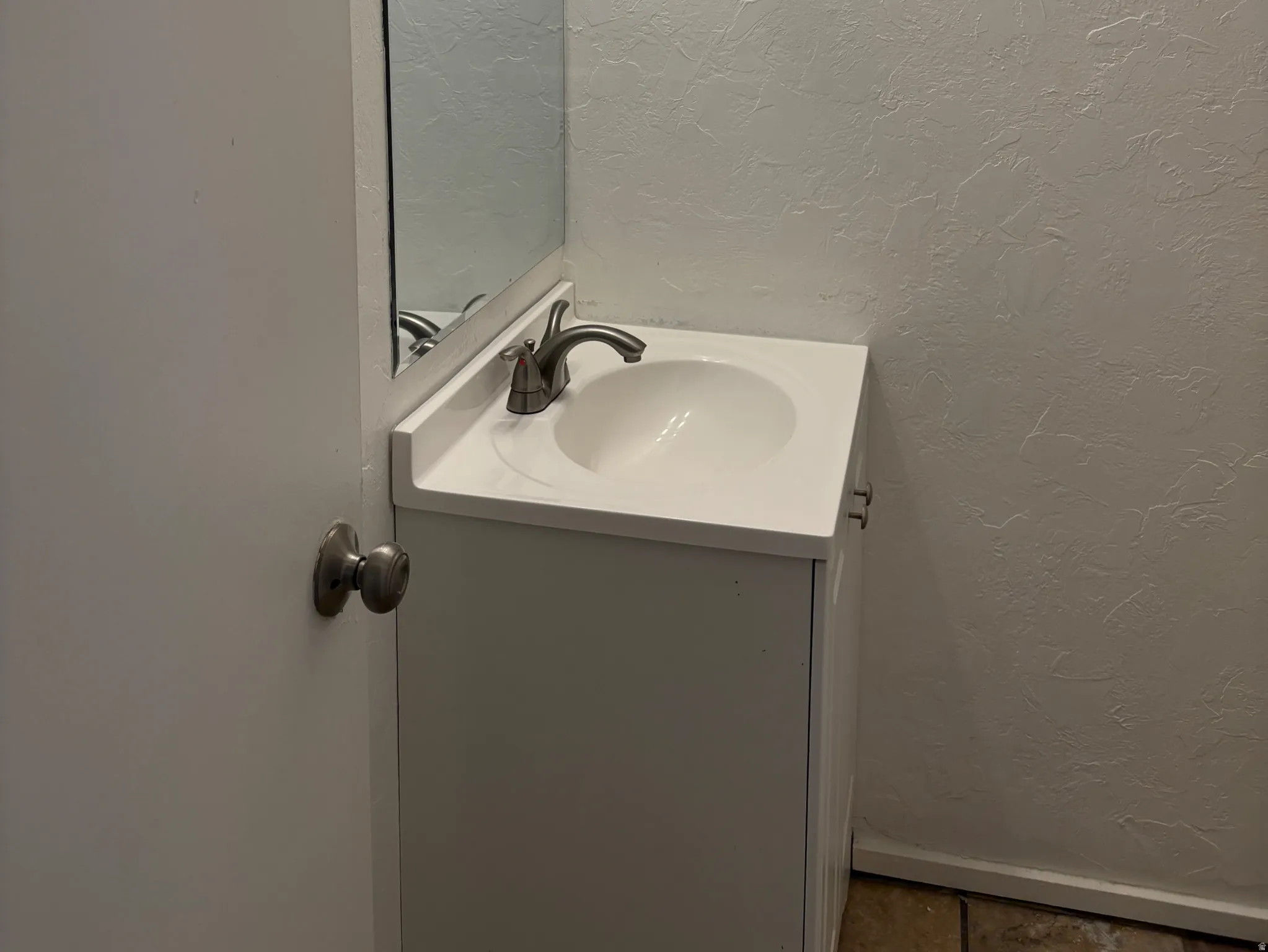 Single vanity with an integrated white sink and brushed nickel faucet, a rectangular mirror, and a three-bulb vanity light fixture