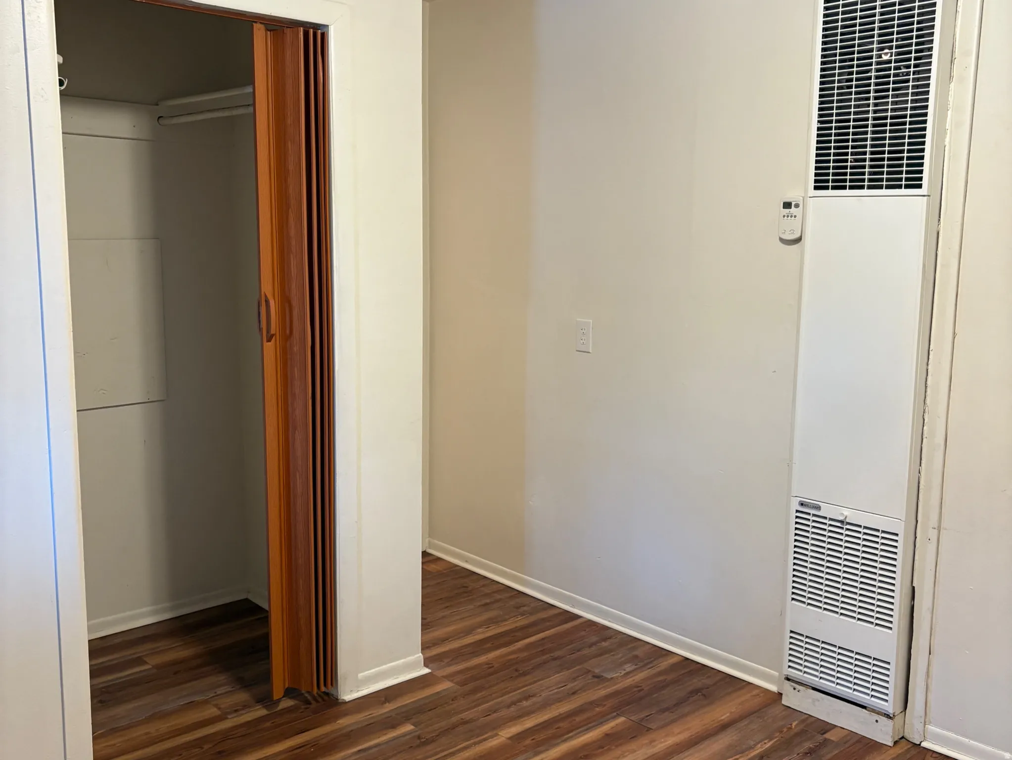 Wood-finish flooring throughout, featuring a wall-mounted heating unit and a closet with bifold doors