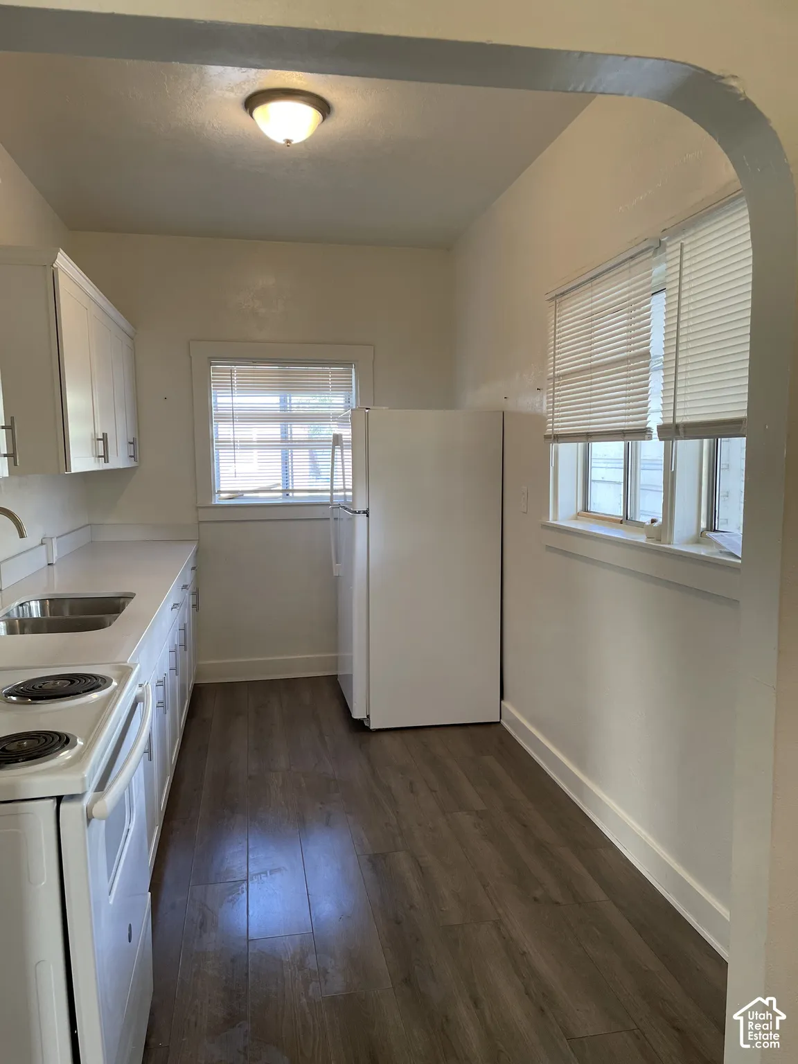 Kitchen featuring wood-finish flooring, white cabinetry with silver-tone hardware, a stainless steel double basin sink, and a white refrigerator