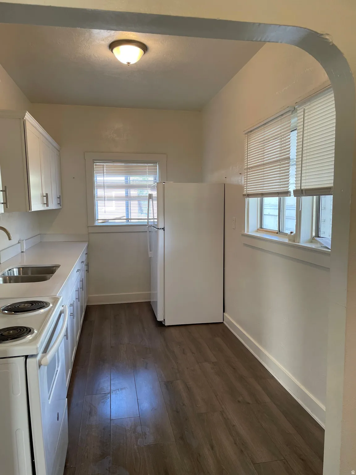 Kitchen featuring wood-finish flooring, white cabinetry with silver-tone hardware, a stainless steel double basin sink, and a white refrigerator
