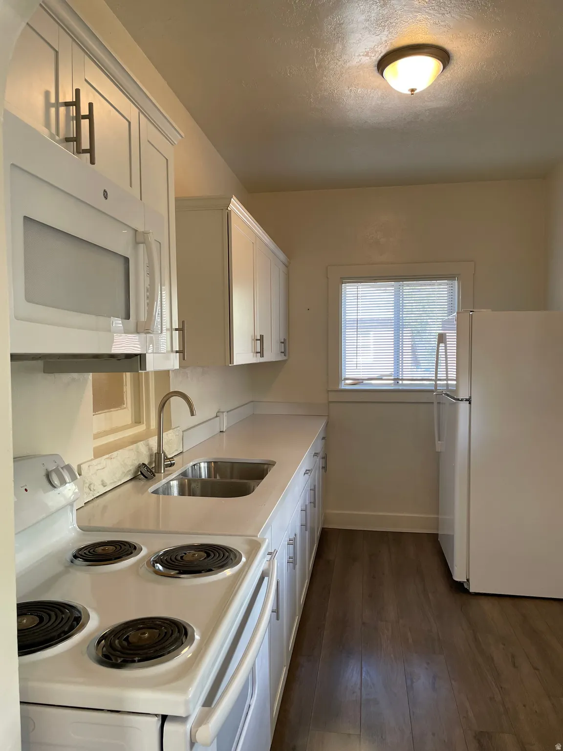 Kitchen featuring white cabinetry with dark hardware, a white oven, a stainless steel double basin sink, and wood-finish flooring