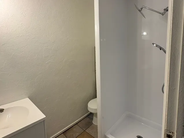 Compact bathroom featuring a white vanity with integrated sink, coordinating toilet, and a stand-up shower with a multi-function showerhead