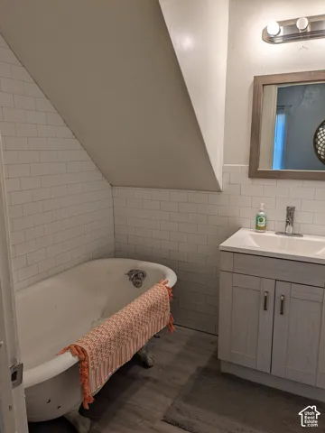 Clawfoot tub with subway tile surround, complementing a vanity with an integrated sink and wood-finish flooring