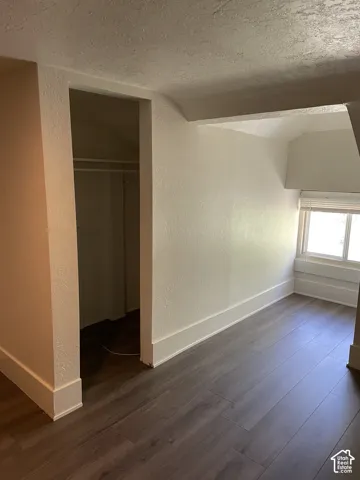 Room featuring wood-finish flooring, white baseboards, light-colored walls, and a window with blinds