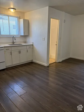Kitchen area featuring dark wood-finish flooring, white cabinetry, light-toned countertops, and a stainless steel gooseneck faucet